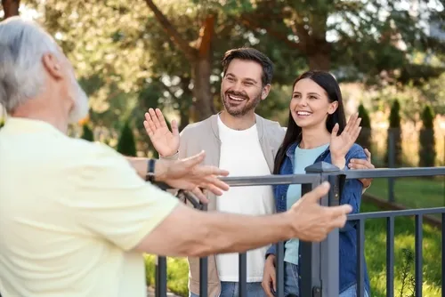 happy couple greeting senior man near fence outdoors